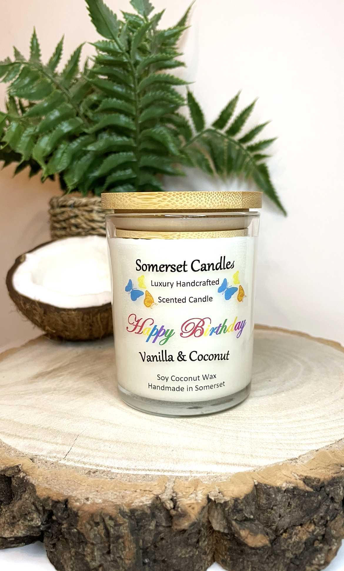 White soy candle in a 7oz clear glass jar with a natural wooden lid. The candle is made from a soy-coconut blend and scented with vanilla and coconut. Above the scent name on the label, several yellow, orange and blue butterflies are displayed, adding a romantic touch. Clean, minimalist design ideal for gifts, home decor or self-care.