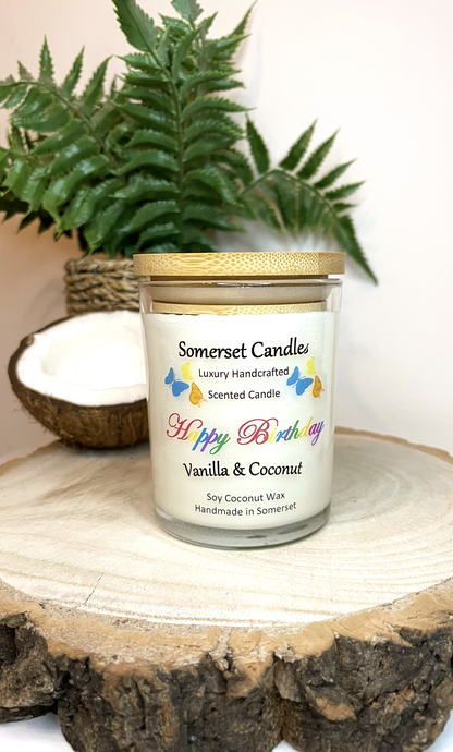 White soy candle in a 7oz clear glass jar with a natural wooden lid. The candle is made from a soy-coconut blend and scented with vanilla and coconut. Above the scent name on the label, several yellow, orange and blue butterflies are displayed, adding a romantic touch. Clean, minimalist design ideal for gifts, home decor or self-care.