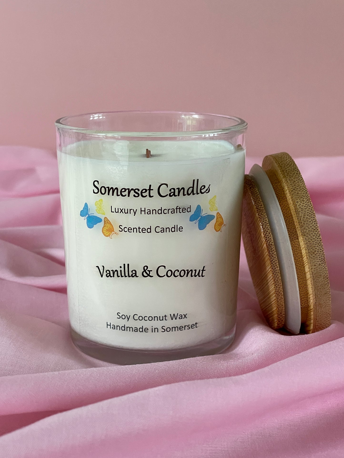 Somerset Candles Vanilla & Coconut candle with a gold lid on a pink fabric background