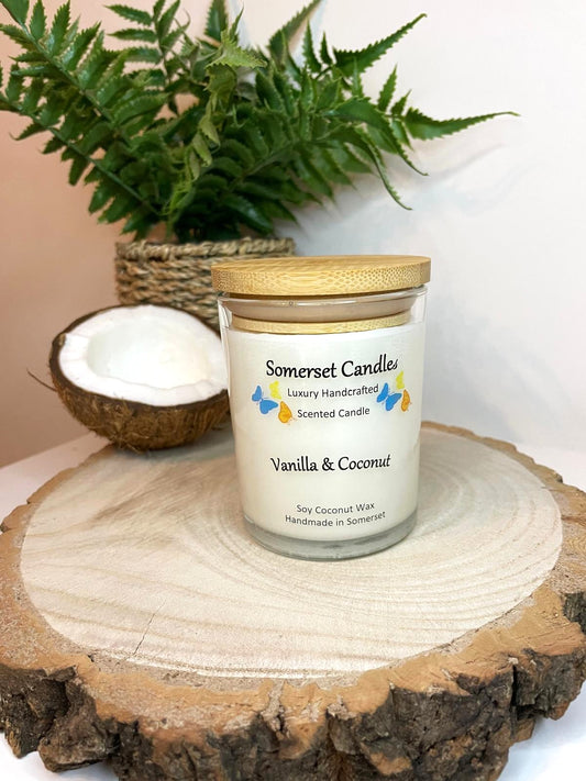 White soy candle in a 7oz clear glass jar with a natural wooden lid. The candle is made from a soy-coconut blend and scented with a fresh scent of vanilla and coconut. Above the scent name on the label, several blue, yellow and orange butterflies are displayed, adding a romantic touch. Clean, minimalist design ideal for gifts, home decor or self-care.
