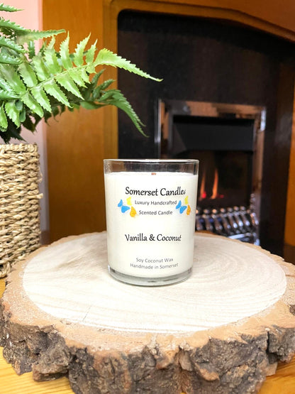 White soy candle in a 7oz clear glass jar with a natural wooden lid. The candle is made from a soy-coconut blend and scented with a fresh scent of vanilla and coconut. Above the scent name on the label, several blue, yellow and orange butterflies are displayed, adding a romantic touch. Clean, minimalist design ideal for gifts, home decor or self-care.