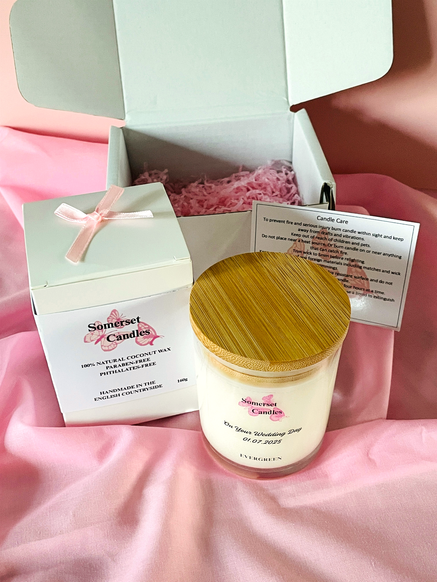Candle with wooden lid and 'Somerset Candles' packaging on a pink fabric background