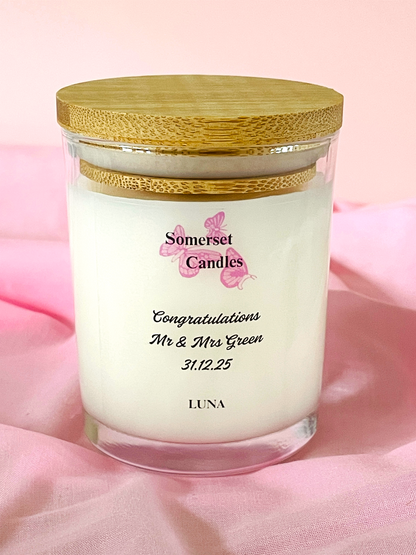 Personalised candle in a glass jar with a wooden lid on a pink fabric background, featuring the brand 'Somerset Candles'.