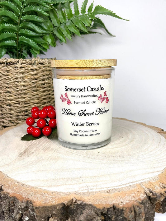 White soy candle in a 7oz clear glass jar with a natural wooden lid. The candle is made from a soy-coconut blend and scented with fruity winter berries. Above the scent name on the label, several red butterflies are displayed, adding a romantic touch. Clean, minimalist design ideal for gifts, home decor or self-care.