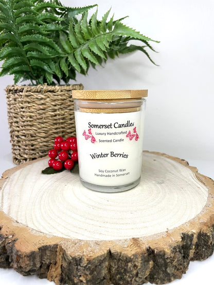 White soy candle in a 7oz clear glass jar with a natural wooden lid. The candle is made from a soy-coconut blend and scented with a fruity scent of winter berries. Above the scent name on the label, several red butterflies are displayed, adding a romantic touch. Clean, minimalist design ideal for gifts, home decor or self-care.