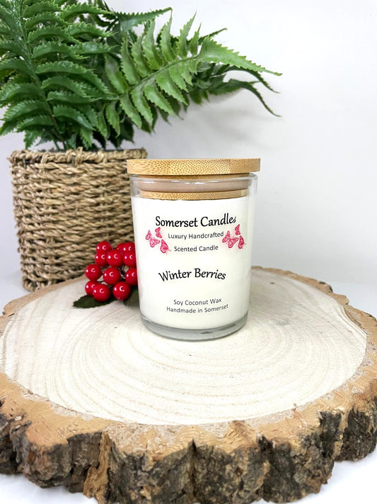 White soy candle in a 7oz clear glass jar with a natural wooden lid. The candle is made from a soy-coconut blend and scented with a fruity scent of winter berries. Above the scent name on the label, several red butterflies are displayed, adding a romantic touch. Clean, minimalist design ideal for gifts, home decor or self-care.