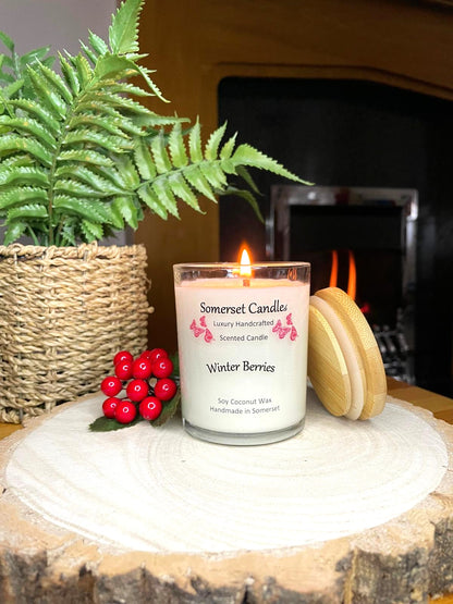 White soy candle in a 7oz clear glass jar with a natural wooden lid. The candle is made from a soy-coconut blend and scented with a fruity scent of winter berries. Above the scent name on the label, several red butterflies are displayed, adding a romantic touch. Clean, minimalist design ideal for gifts, home decor or self-care.