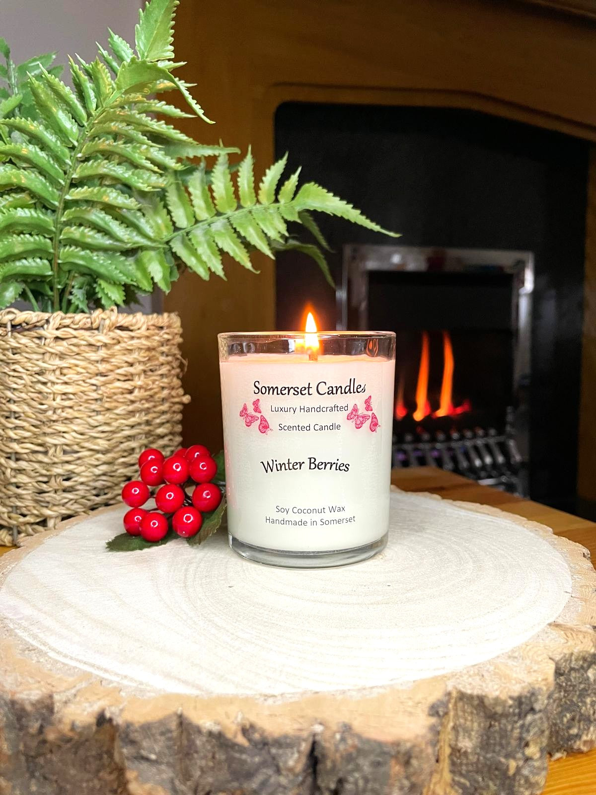 White soy candle in a 7oz clear glass jar with a natural wooden lid. The candle is made from a soy-coconut blend and scented with a fruity scent of winter berries. Above the scent name on the label, several red butterflies are displayed, adding a romantic touch. Clean, minimalist design ideal for gifts, home decor or self-care.