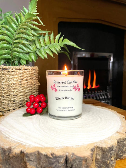 White soy candle in a 7oz clear glass jar with a natural wooden lid. The candle is made from a soy-coconut blend and scented with a fruity scent of winter berries. Above the scent name on the label, several red butterflies are displayed, adding a romantic touch. Clean, minimalist design ideal for gifts, home decor or self-care.