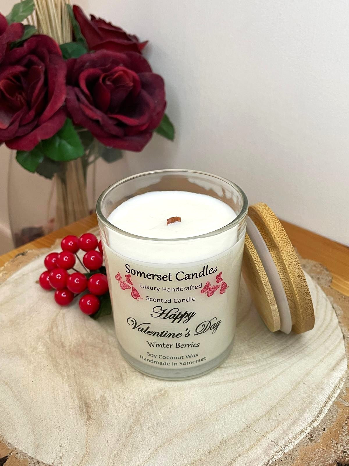 White soy candle in a 7oz clear glass jar with a natural wooden lid. The candle is made from a soy-coconut blend and scented with fruity winter berries. Above the scent name on the label, several red butterflies are displayed, adding a romantic touch. Clean, minimalist design ideal for gifts, home decor or self-care.