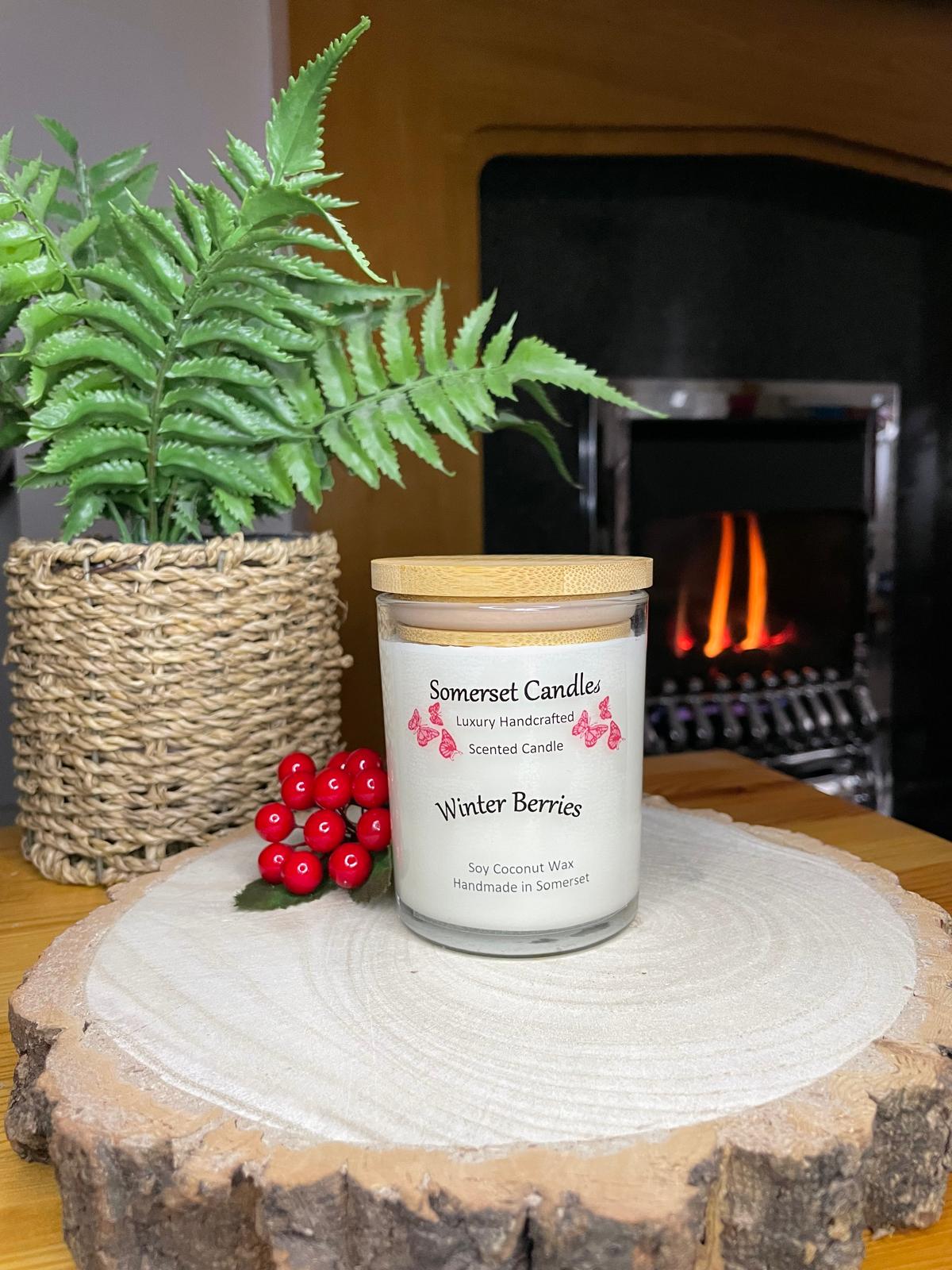 White soy candle in a 7oz clear glass jar with a natural wooden lid. The candle is made from a soy-coconut blend and scented with a fruity scent of winter berries. Above the scent name on the label, several red butterflies are displayed, adding a romantic touch. Clean, minimalist design ideal for gifts, home decor or self-care.