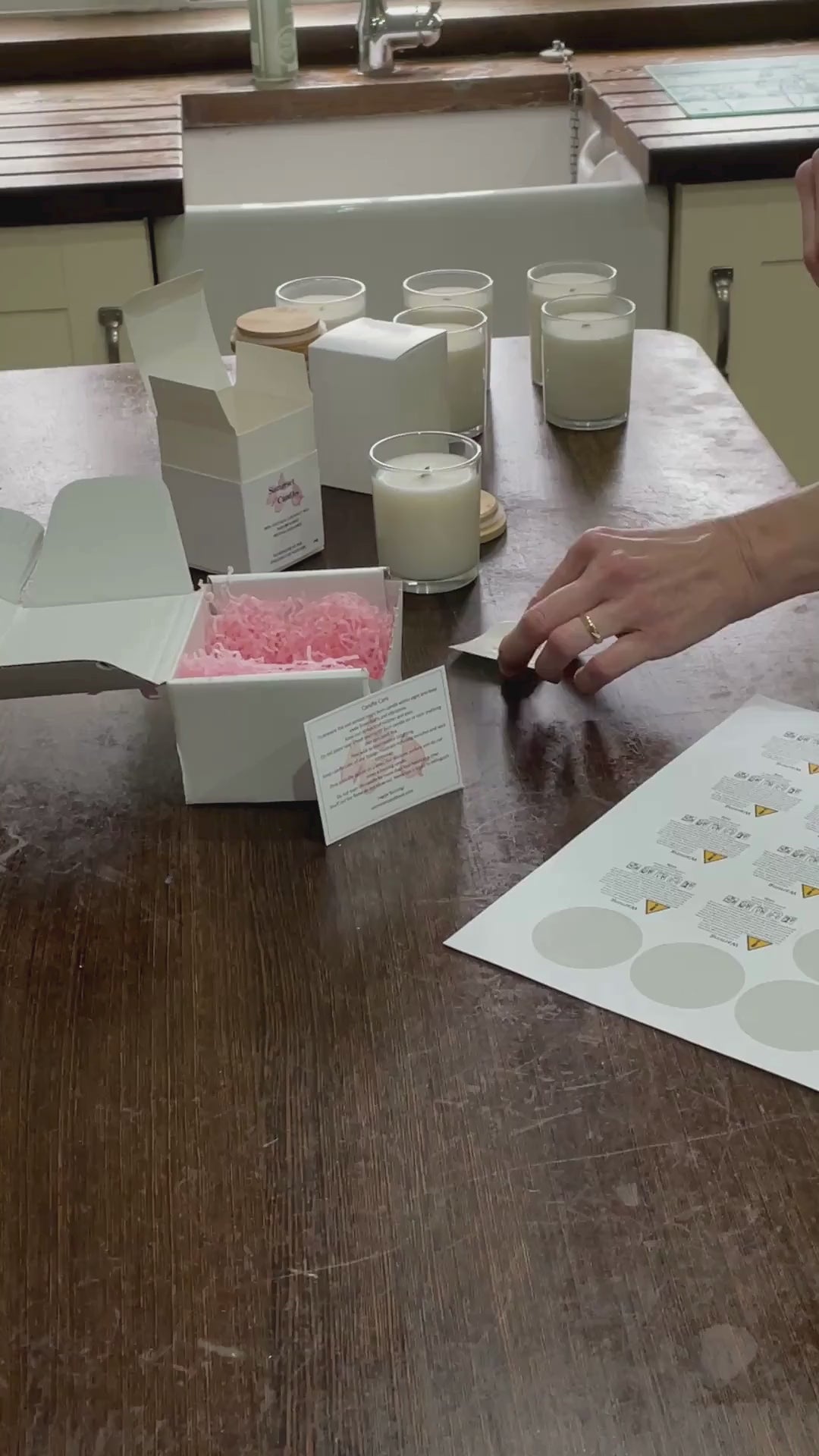 Load video: Video showing the packaging up of an Evergreen candle. Show CLP label and Front label being fitted, placing into the gift box, then being placed into the shipping box with pink shredded tissue paper and a candle care card being placed into the box.